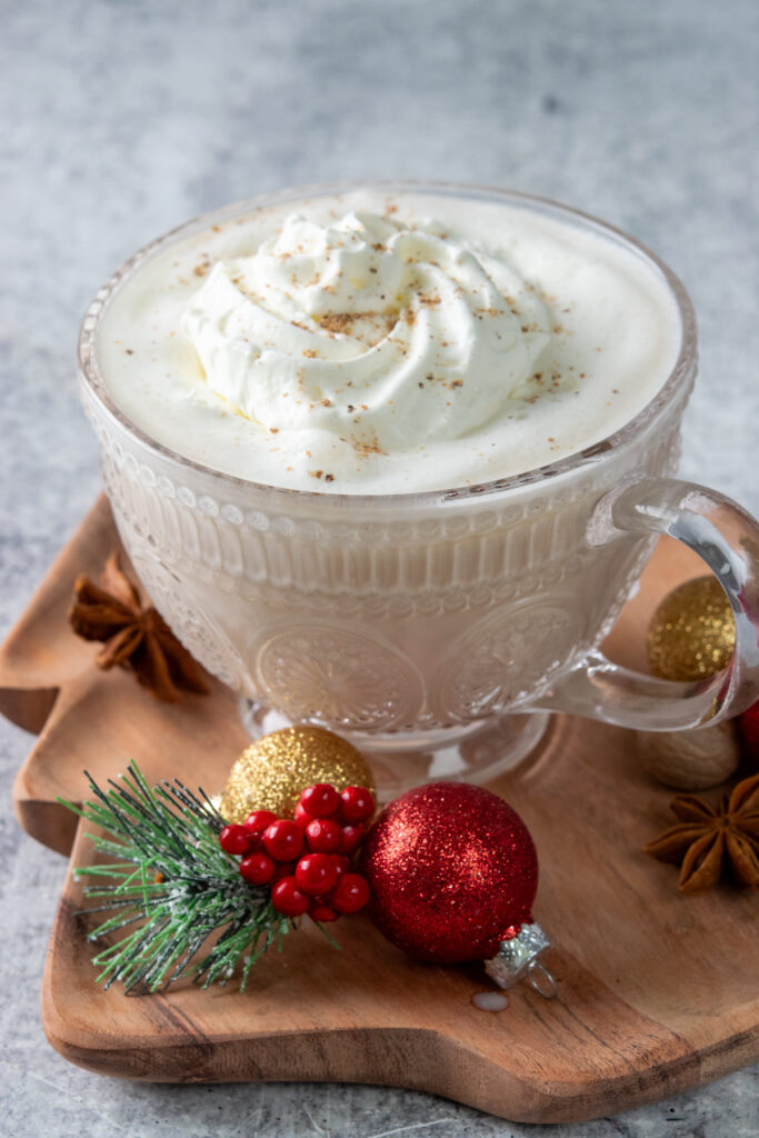 A Christmas Morning Chai made just like Dutch Bros at home. The holiday drink is in a glass mug surrounded by small red and gold Christmas ornaments and a couple star anise, a spice often found in chai.