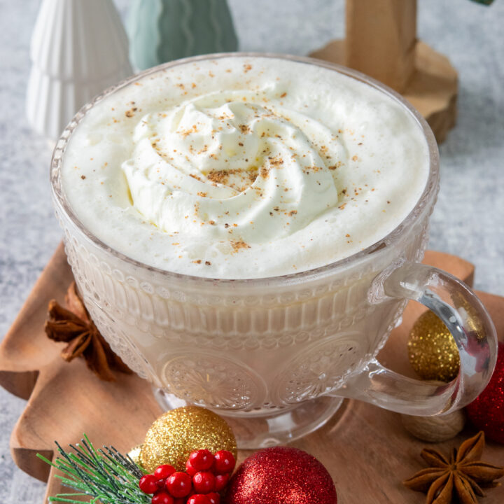 Christmas Morning Chai drink in a mug that's surrounded by colorful Chrismas decorations and small Christmas trees. This Dutch Bros copycat chail latte is holiday-ready with creamy whipped cream and nutmeg sprinkled on top.
