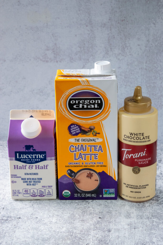 The three ingredients needed to make a homemade Dutch Bros Christmas Morning Chai in their packages. There's a small carton of half and half. A carton of Oregon Chai Tea Latte concentrate, and a bottle of Torani white chocolate sauce.