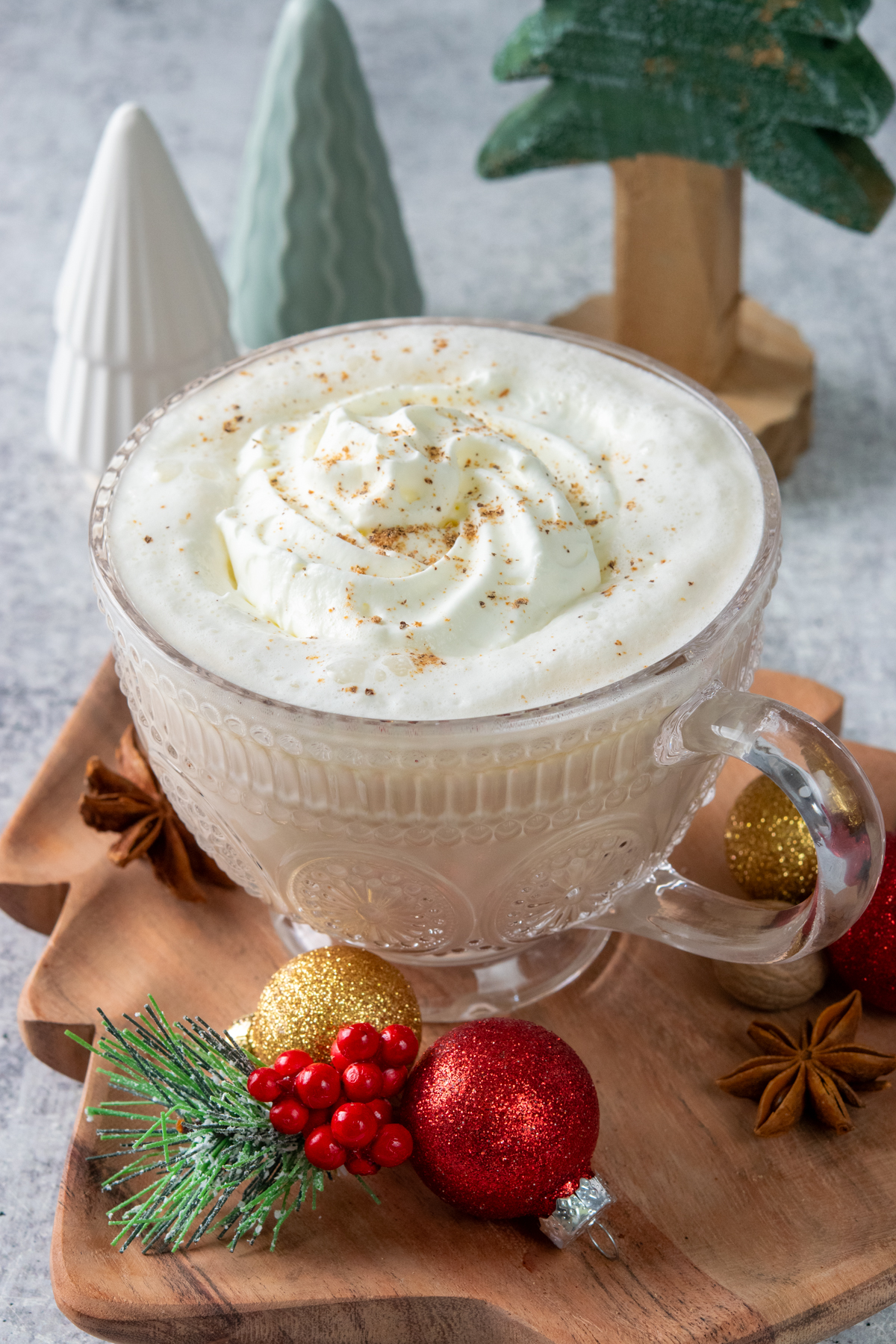 Christmas Morning Chai drink in a mug that's surrounded by colorful Chrismas decorations and small Christmas trees. This Dutch Bros copycat chail latte is holiday-ready with creamy whipped cream and nutmeg sprinkled on top.