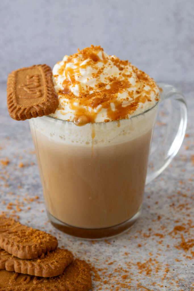 A cookie butter latte topped with crushed Biscoff cookie crumbs and homemade cookie butter sauce on a big dollop of whipped cream.