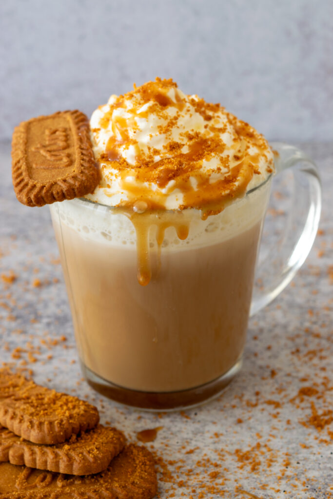 Homemade cookie butter latte with a Biscoff Lotus cookie sitting in the whipped cream which has cookie crumbs sprinkled on it along with some cookie butter sauce.