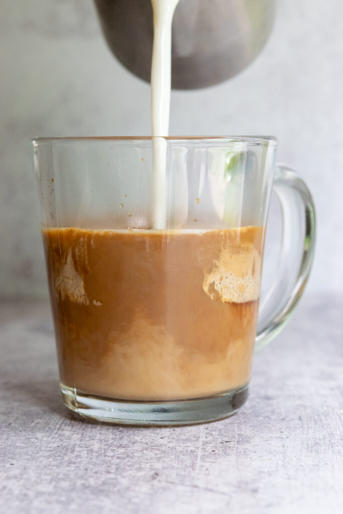 Pouring steamed milk into a mug with espresso and cookie butter to make a cookie butter latte.