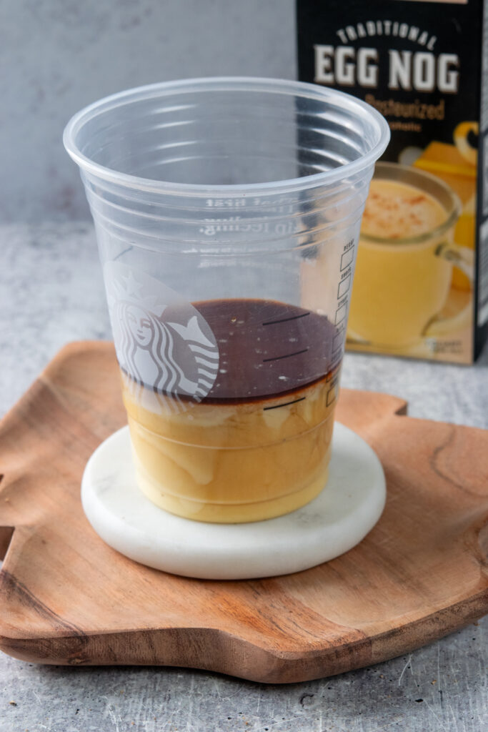 Using a Starbucks cold cup to measure the concentrated coffee and eggnog before pouring it into the blender to make a frappuccino. There's a carton of eggnog behind the cup.