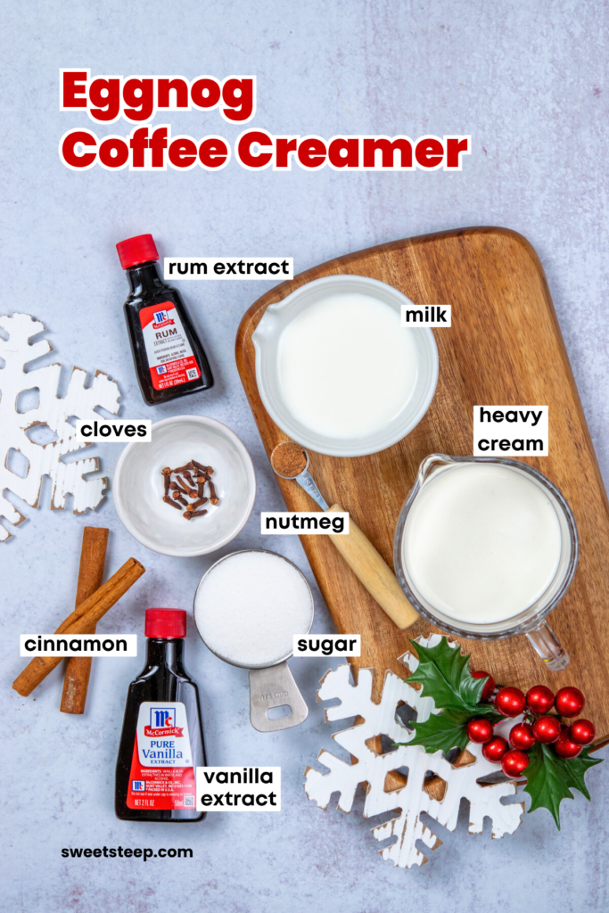 Overhead image showing the ingredients needed to make eggnog coffee creamer. There's are bottles of rum and vanilla extracts, pitchers of milk and heavy cream, whole cloves, cinnamon sticks, ground nutmeg and sugar. The image has text overlay that reads, "eggnog coffee creamer" and has a few snowflake ornaments on it since you would make this creamer in the winter.