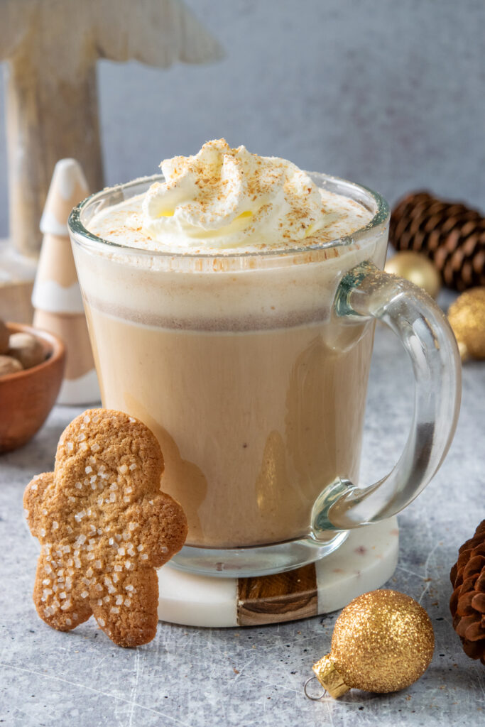 A gingerbread chai latte in a mug with a gingerbread cookie next to it.