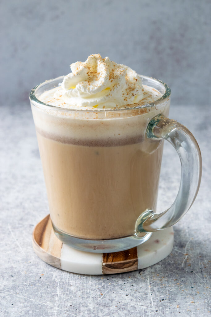 A hot gingerbread chai latte in a cozy mug with a topping of whipped cream and garnish of freshly grated nutmeg.