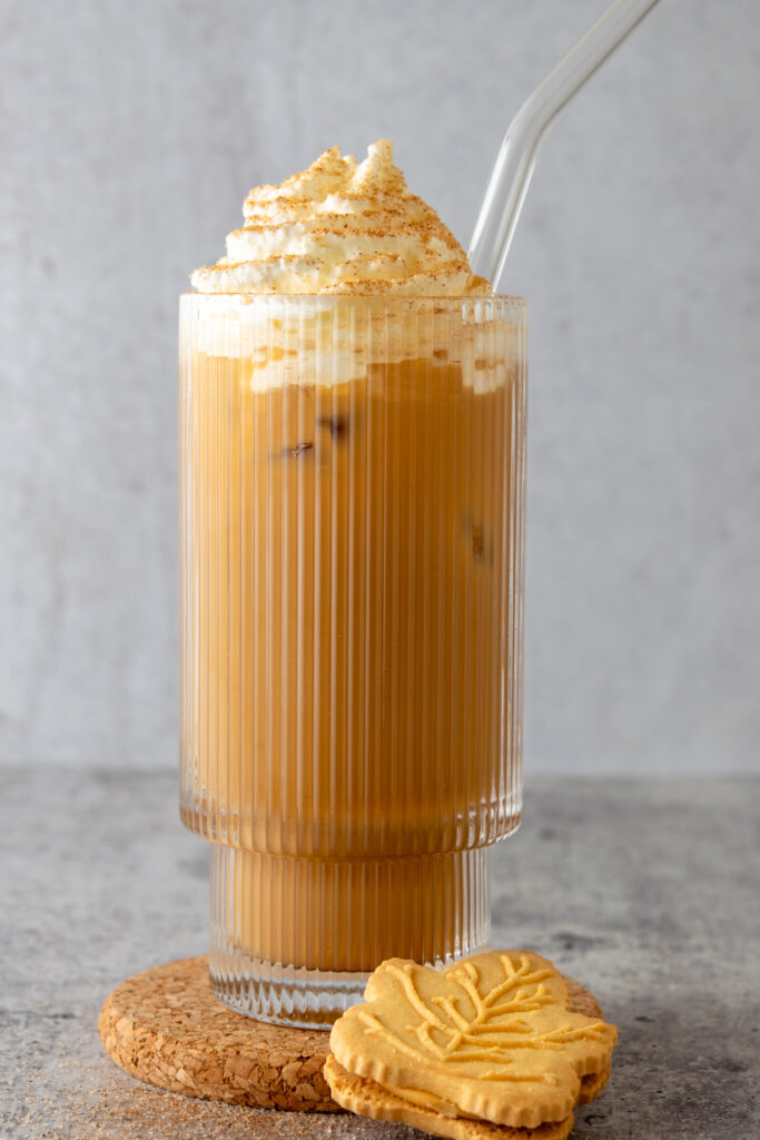 An iced maple latte in a glass cup with glass straw and a maple syrup cookie sitting next to it.