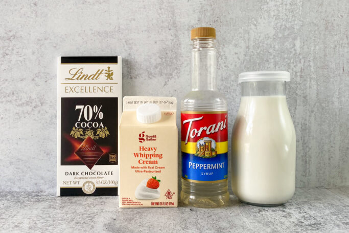 All the ingredients for making peppermint mocha coffee creamer in their packages, including Lindt 70% dark cocoa chocolate bar, carton of heavy whipping cream, bottle of Torani peppermint syrup and bottle of whole milk.