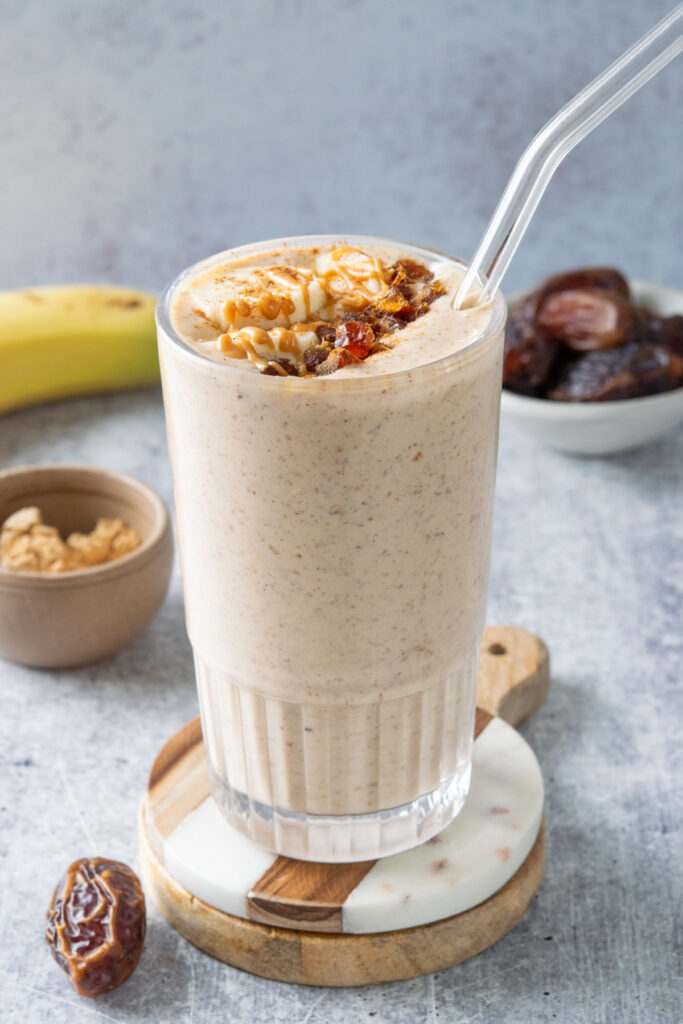 Peanut butter banana date smoothie that's garnished with banana slices and chopped dates, sprinkled with cinnamon and peanut butter drizzled on top. The smoothie is thick and creamy with flecks of Medjool dates in it.