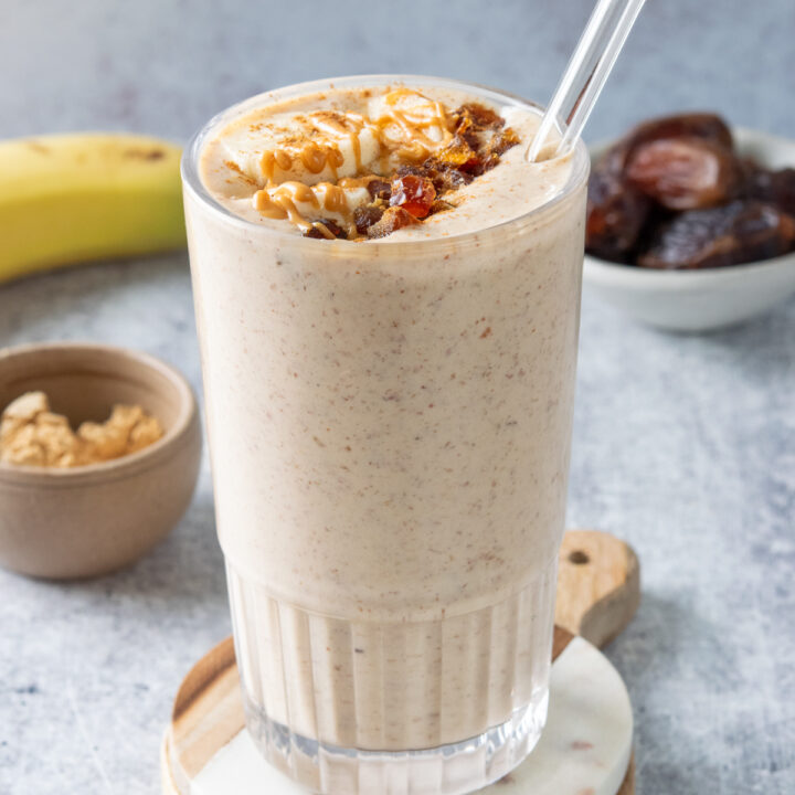 Peanut butter banana date smoothie that's garnished with banana slices and chopped dates, sprinkled with cinnamon and peanut butter drizzled on top. The smoothie is thick and creamy with flecks of Medjool dates in it.