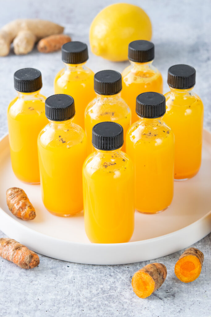 Homemade turmeric shots in eight small two-ounce bottles, next to some fresh turmeric root.