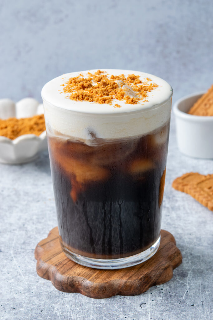 A Dunkin' Donuts copycat cookie butter cold brew coffee with layers of cold brew and ice topped with creamy cookie butter cold foam, crushed Biscoff cookies, and whole Lotus Biscoff cookies on the side.