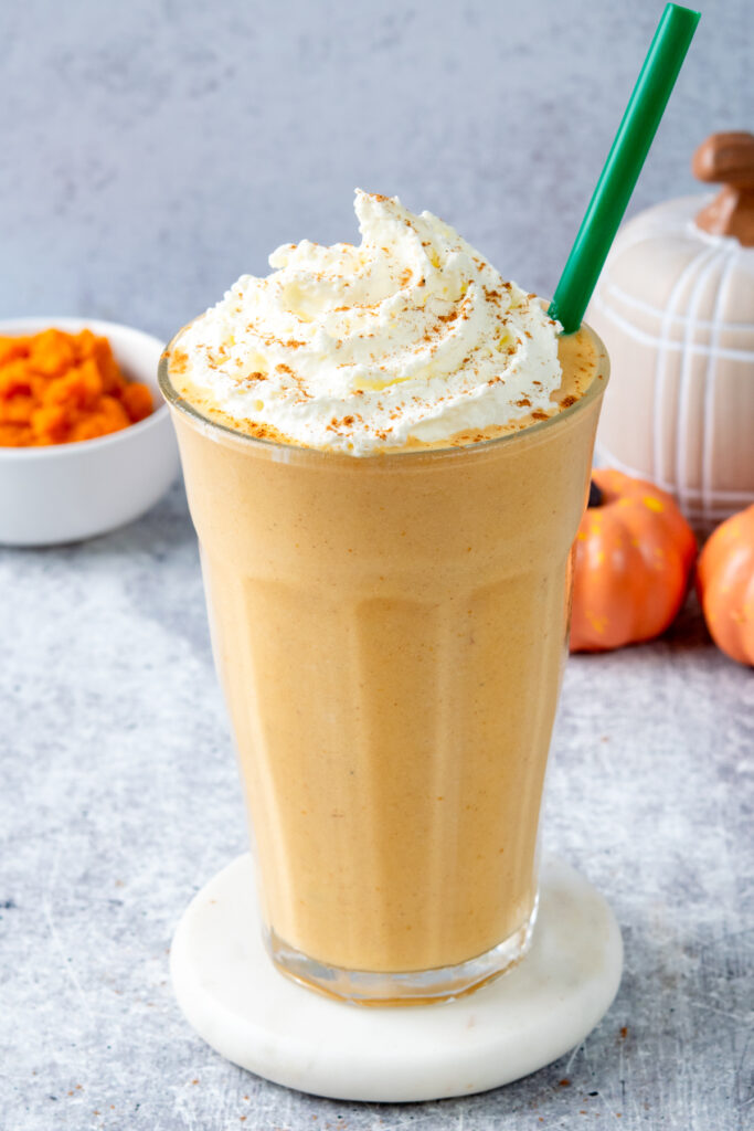Copycat Starbucks Pumpkin Spice Crème Frappuccino topped with whipped cream in a tall glass with a green straw, made without coffee for a caffeine-free fall treat.