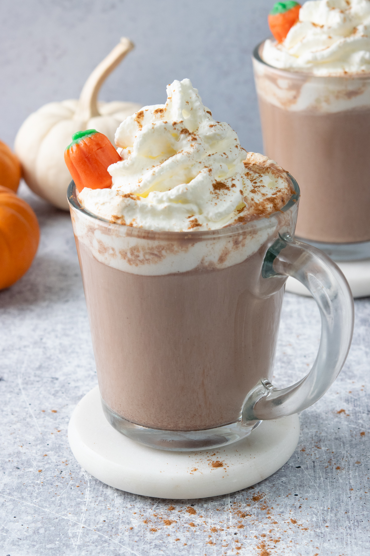 Pumpkin spice hot chocolate topped with whipped cream, pumpkin pie spice, and a pumpkin candy garnish.